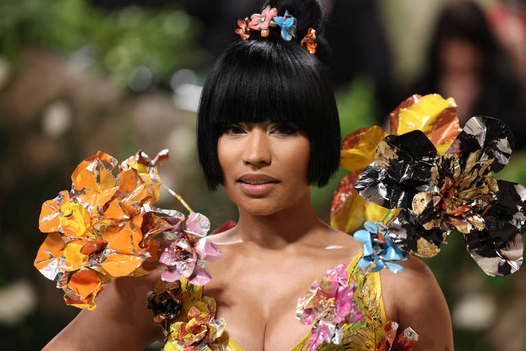 Nicki Minaj veste roupa amarela com grandes detalhes nos ombros enquanto posa para foto no tapete vermelho.