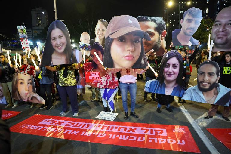 Pessoas seguram fotos de rostos de reféns em uma manifestação