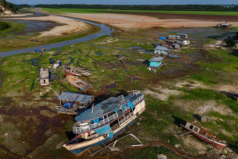 Barcos encalhados em margem de um curso de água com grandes bancos de areia e muito limo no solo