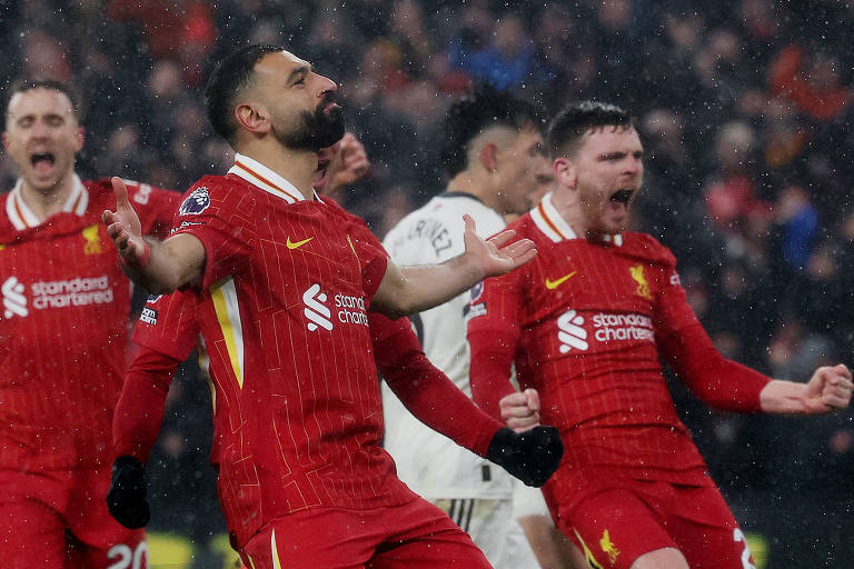 O egípcio Salah， ladeado pelo português Jota e pelo escocês Robertson， comemora seu gol em Liverpool versus Manchester United， na Premier League; todos usam uniforme vermelho