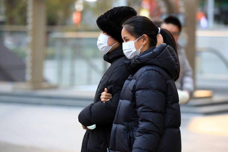 Duas pessoas caminham na rua usando máscaras de proteção da boca e nariz