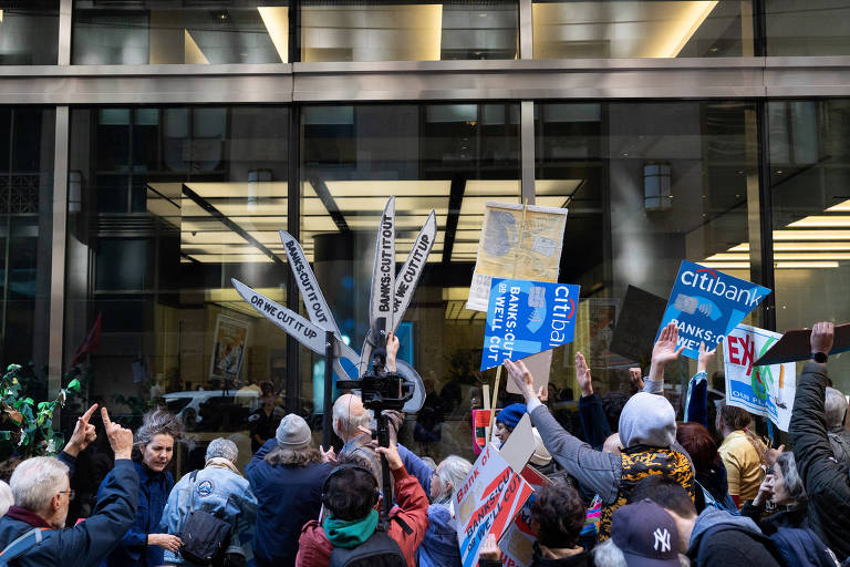 Pessoas protestam com cartazes com o nome do Citibank na frente de um prédio envidraçado