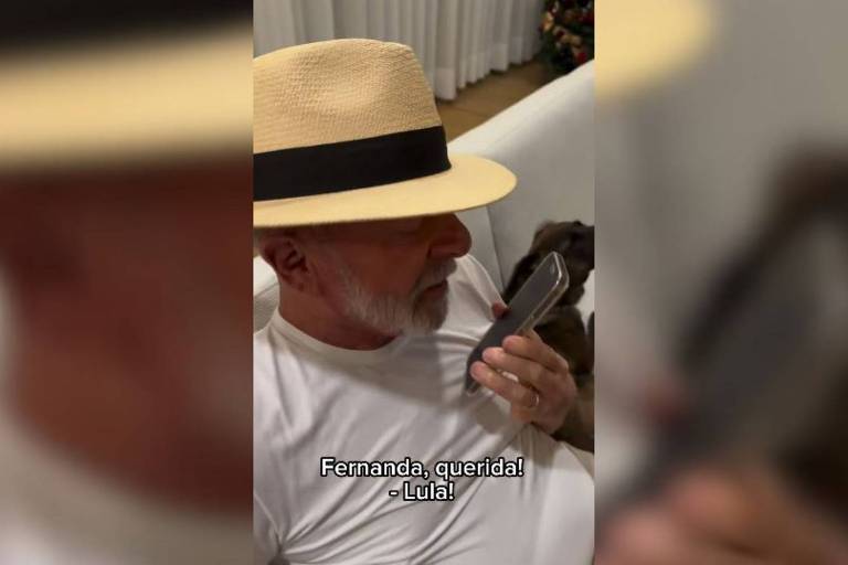 O presidente Lula está com um chapéu Panamá e uma camiseta branca， enquanto segura um telefone celular com a mão esquerda próxima à boca. Ele está sentado em um sofá. Há uma legenda na imagem que diz: quot;Fernanda， queridaquot;. 