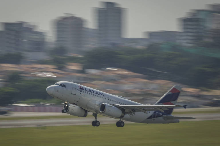 Um avião está decolando em uma pista， com a cidade ao fundo. O avião está inclinado para cima， com as rodas ainda na pista. Ao fundo， há prédios e uma área urbana.