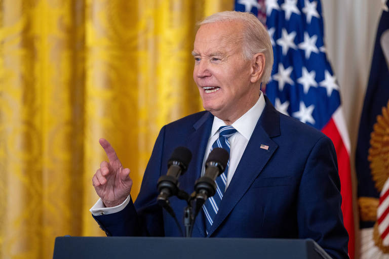 Biden fala ao microfone em palanque; ele aponta com um dedo enquanto fala; ao fundo， há uma bandeira dos EUA