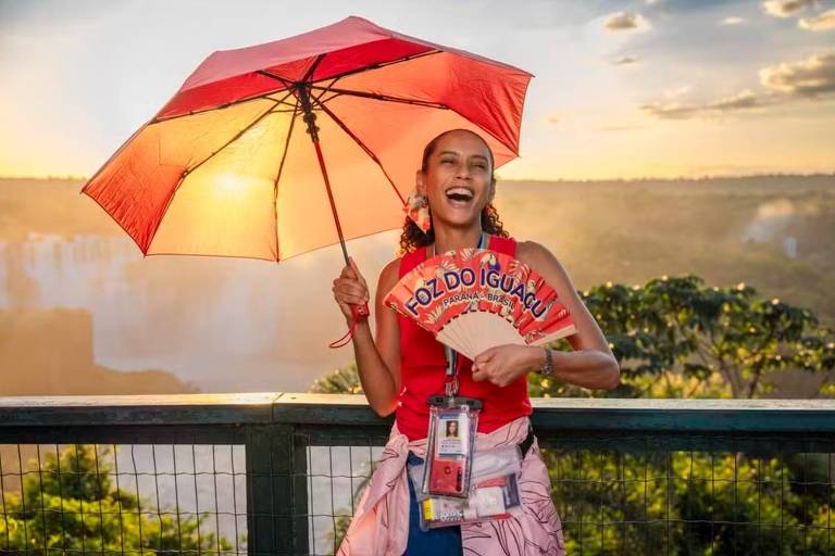 Em foto colorida, mulher sorri e posa para foto em ponto turístico