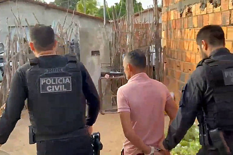 Imagem mostra dois agentes da Polícia Civil de uniforme preto enquanto Francisco está de costas， com uma camisa rosa， e algemado 