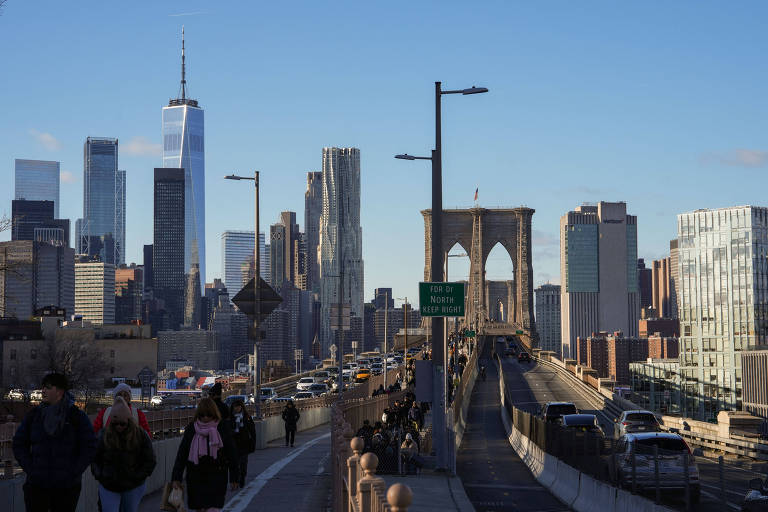 fotografia colorida mostra carros em uma ponte. ao fundo, é possível ver a os arranha-céus característicos do distrito financeiro e comercial de Nova York 