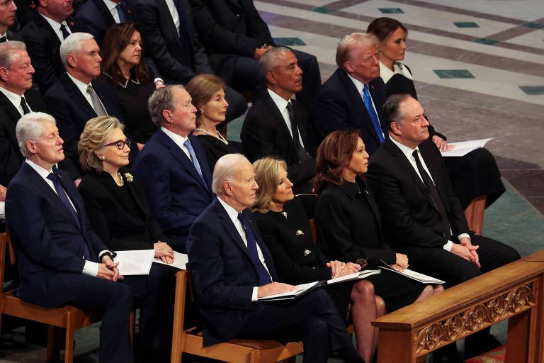 A imagem mostra um grupo de líderes políticos sentados em bancos de madeira em um ambiente formal. Todos estão vestidos de maneira formal， muitos usando roupas escuras， sugerindo um evento solene