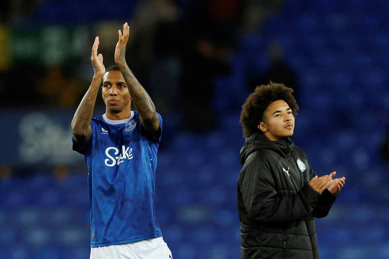 Ashley Young， próximo ao filho Tyler， depois da partida entre Everton e Peterborough， em Liverpool， pela Copa da Inglatrerra; eles estão de costas um para o outro， Ashley com a camisa azul do Everton e Tyler com agasalho preto， e agradecem à presença da torcida no estádio Goodison Park