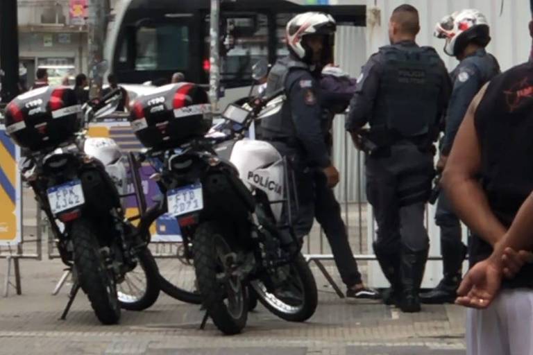 Imagem mostra três policiais militares e duas motos em uma cena urbana