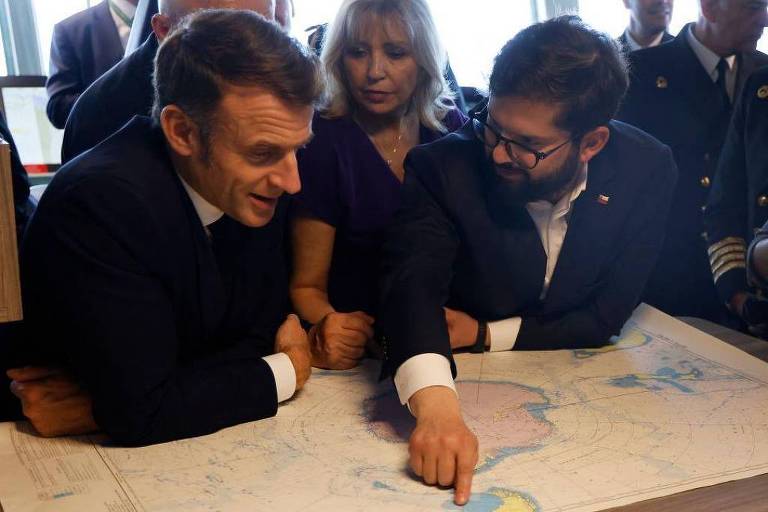 Foto mostra dois homens brancos， o presidente francês， Emmanuel Macron， e o chileno， Gabriel Boric olhando e conversando para um mapa da Antártida sobre uma mesa. 