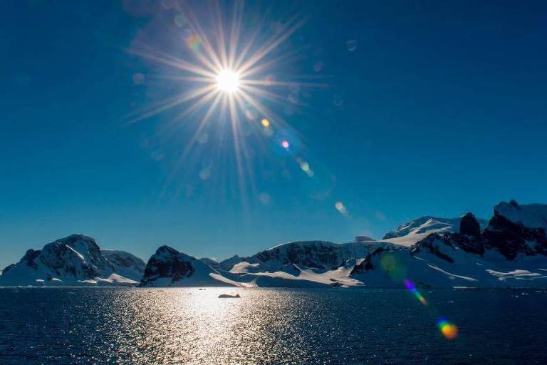 Foto mostra sol brilhando no céu azul do Polo Sul， sobre o mar da região