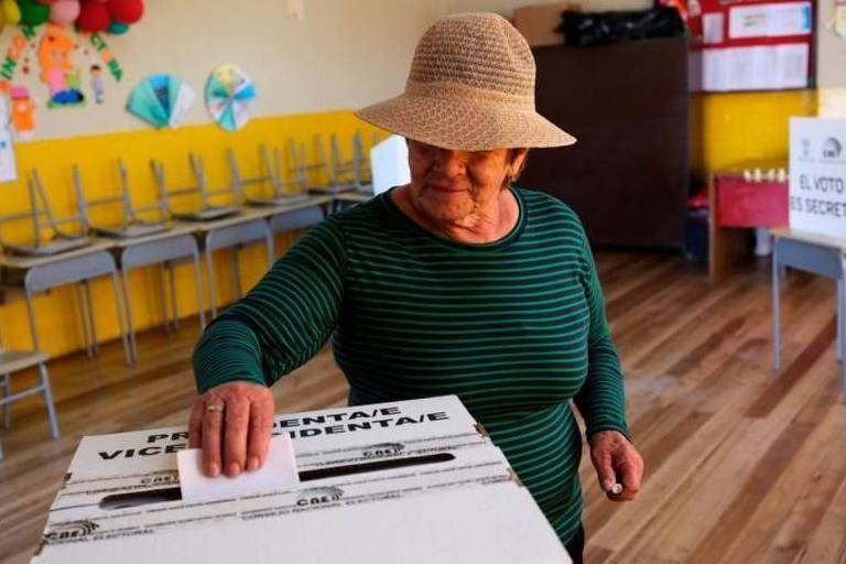 Mulher com chapéu deposita voto em urna em escola