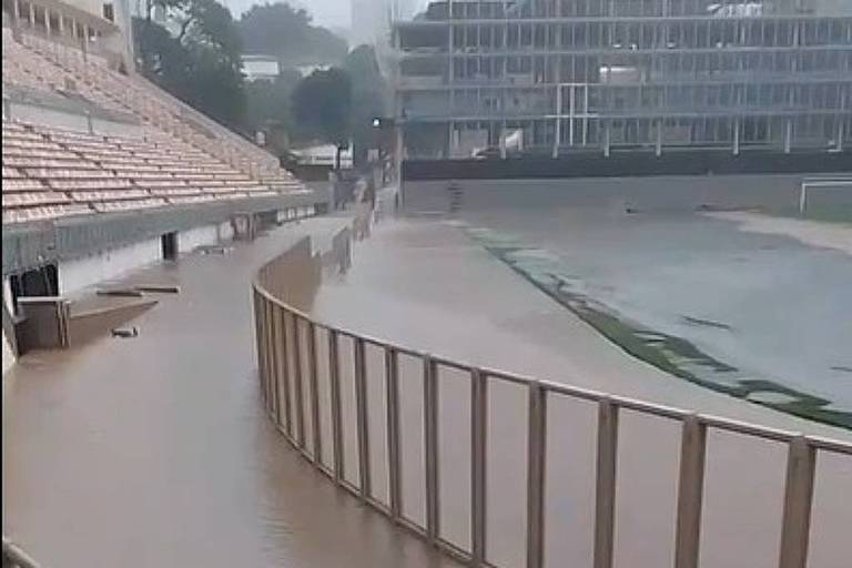 Imagem do estádio do Pacaembu alagado， com água barrenta cobrindo área entre o gramado e a arquibancada