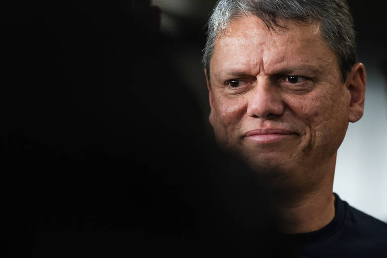 A imagem mostra um homem com cabelo curto e grisalho， sorrindo levemente. O fundo é desfocado， destacando o rosto do homem