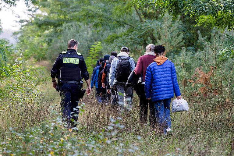 Um oficial da Polícia Federal Alemã (Bundespolizei) escolta um grupo de migrantes perto de Forst， no leste da Alemanha， em 11 de outubro de 2023， durante patrulha perto da fronteira com a Polônia