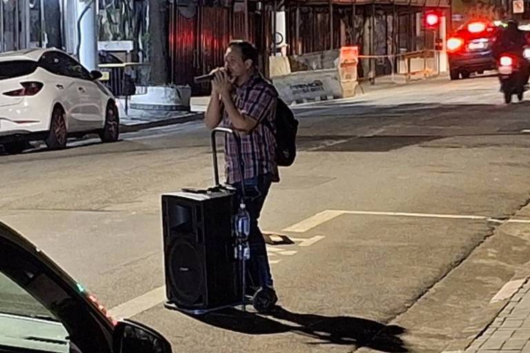 Em foto colorida， um cantor passa cantando pelas ruas do bairro de Perdizes， em São Paulo， mostrando sua arte 