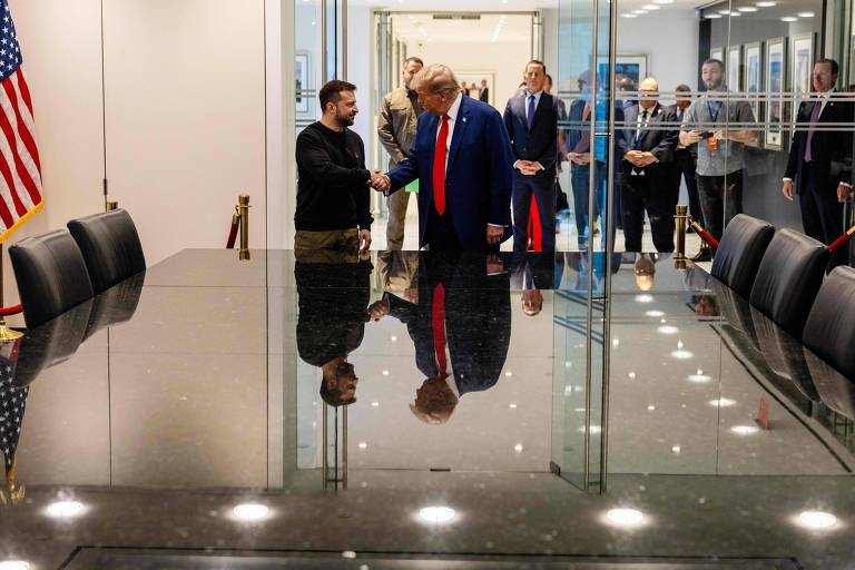 A imagem mostra um encontro entre duas pessoas que estão se cumprimentando em uma sala de reuniões. À esquerda， há uma bandeira dos Estados Unidos. A mesa de reuniões é grande e escura， refletindo a luz do ambiente. Ao fundo， várias pessoas observam a cena， algumas em pé e outras sentadas. O ambiente é bem iluminado e moderno.