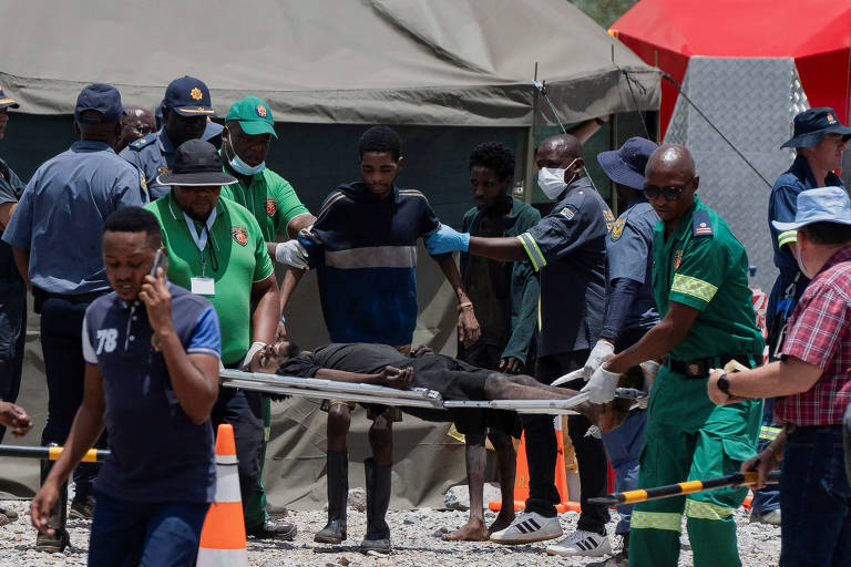 A imagem mostra uma equipe de resgate em uma situação de emergência. Várias pessoas estão ao redor de uma maca， onde um corpo está sendo transportado. Os membros da equipe estão vestidos com uniformes de resgate e há uma tenda ao fundo. Algumas pessoas estão usando máscaras， e há cones de sinalização no chão