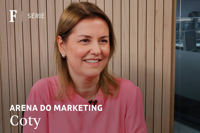 A imagem mostra uma mulher sorridente com cabelo castanho claro， usando uma blusa rosa. Ela está sentada em um ambiente com paredes de madeira ao fundo. Na parte inferior da imagem， há texto que diz 039;ARENA DO MARKETING039; e 039;Coty039;.