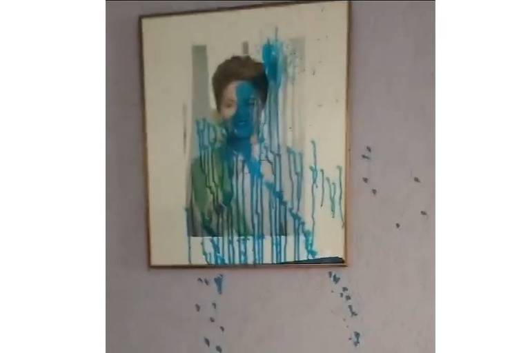 A imagem mostra um quadro pendurado na parede， onde a pintura foi coberta com tinta azul que escorre. A tinta parece ter sido derramada de forma desordenada， criando um efeito de gotejamento. O fundo da imagem é uma parede clara.