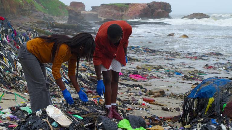 Praia de Gana, na África, tomada por lixo têxtil, em cena do documentário "Buy Now: The Shopping Conspiracy", produzido pela Netflix. Gana recebe doações e descartes de vestuário vindo da Europa, EUA e China e parte desses itens vai parar em rios e praias do país