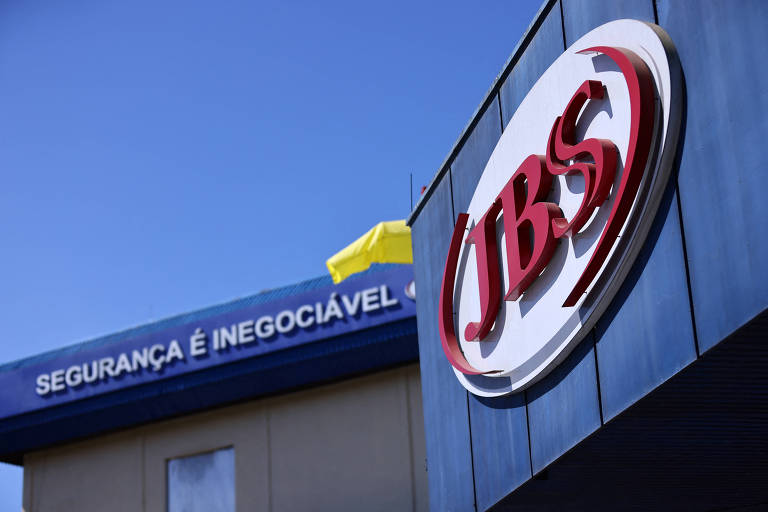 A imagem mostra a fachada de um edifício da JBS. No topo, há uma faixa azul com a frase 'SEGURANÇA É INEGOCIÁVEL'. O logotipo da JBS, em vermelho, está em destaque na lateral do edifício, que possui uma estrutura moderna e limpa sob um céu azul.