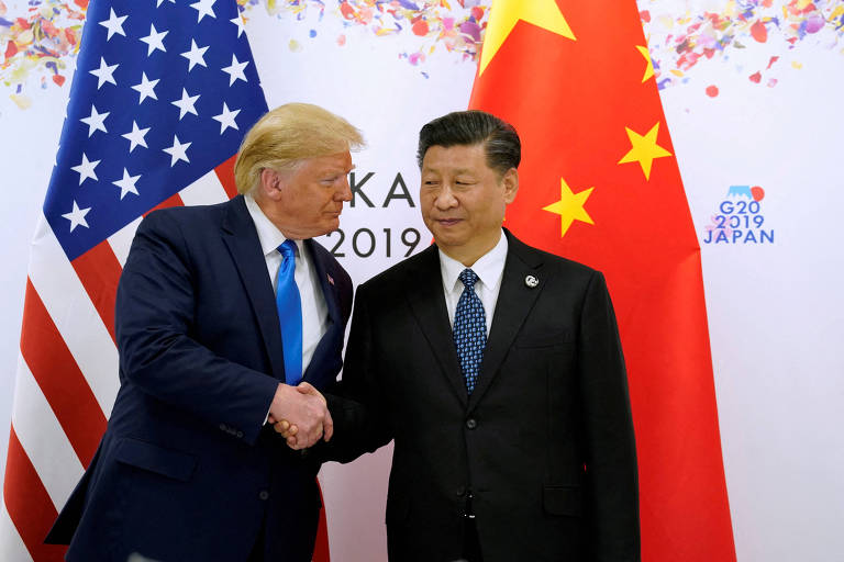 A imagem mostra dois homens apertando as mãos em um evento. À esquerda， há uma bandeira dos Estados Unidos e， à direita， uma bandeira da China. O fundo é decorado com confetes coloridos. Os homens estão vestidos formalmente， um com um terno escuro e gravata clara， e o outro com um terno escuro e gravata azul. A data 039;G20 2019 Japão039; está visível no fundo.