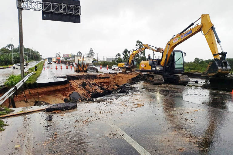 Foto mostra abertura de uma cratera na BR-101， na altura de Biguaçu， na Grande Florianópolis. Uma máquina opera no local. Situação foi registrada após fortes chuvas em Santa Catarina. 
