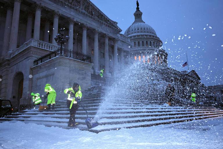 Capitólio dos EUA com neve nas escadas e trabalhadores tirando com equipamentos próprios