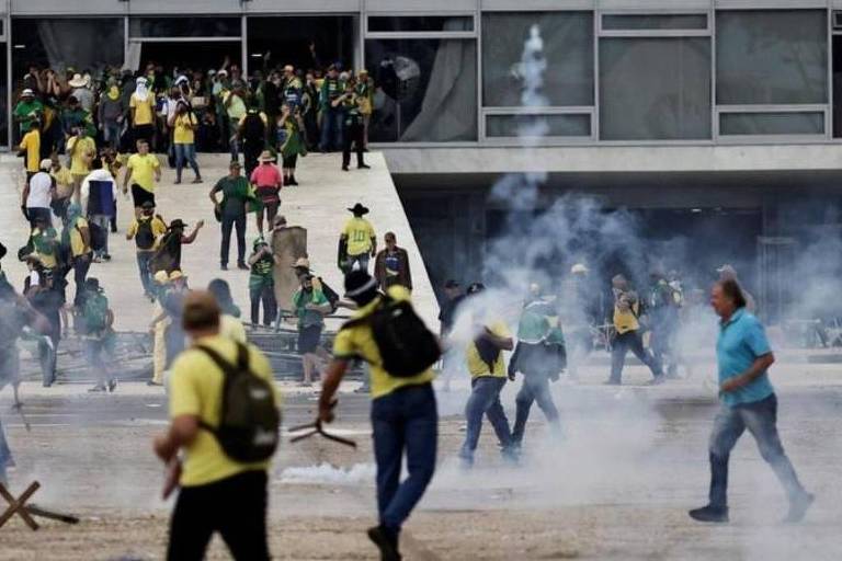 A imagem mostra um protesto em Brasília, com várias pessoas vestindo camisetas amarelas e algumas em camisetas verdes. Há fumaça no ar, possivelmente de bombas de gás lacrimogêneo, e as pessoas parecem estar se dispersando ou correndo. Ao fundo, um grupo de manifestantes está subindo as escadas de um edifício.