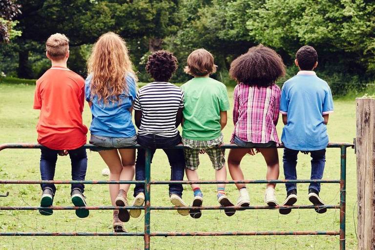 Um grupo muito diversificado de crianças sentadas em cima do muro
