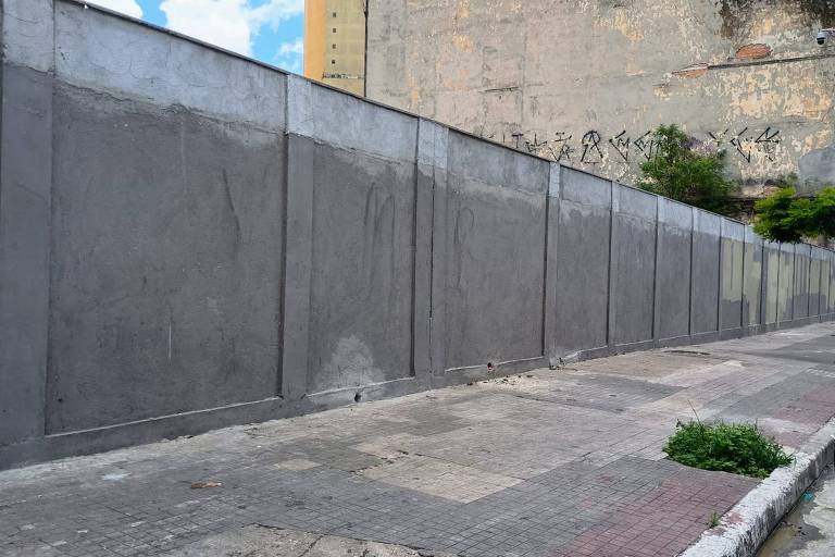 Imagem mostra um muro de concreto ao lado de uma calçada