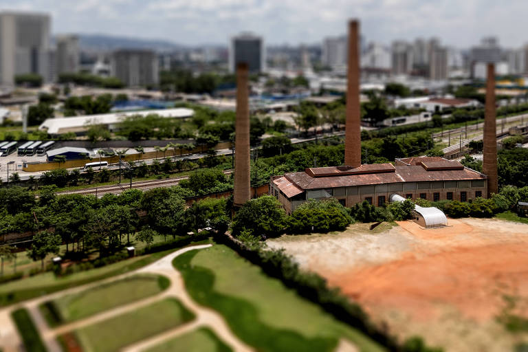 Casa das Caldeiras com gramado e terreno arenoso à frente e cenário urbano ao fundo