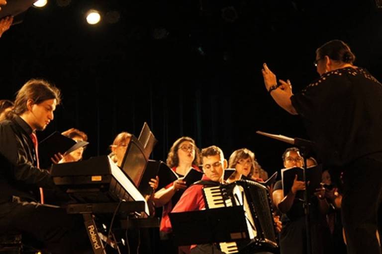 Em foto colorida， integrantes do CORALUSP aparecem cantando sob regência de Márcia Montesanti