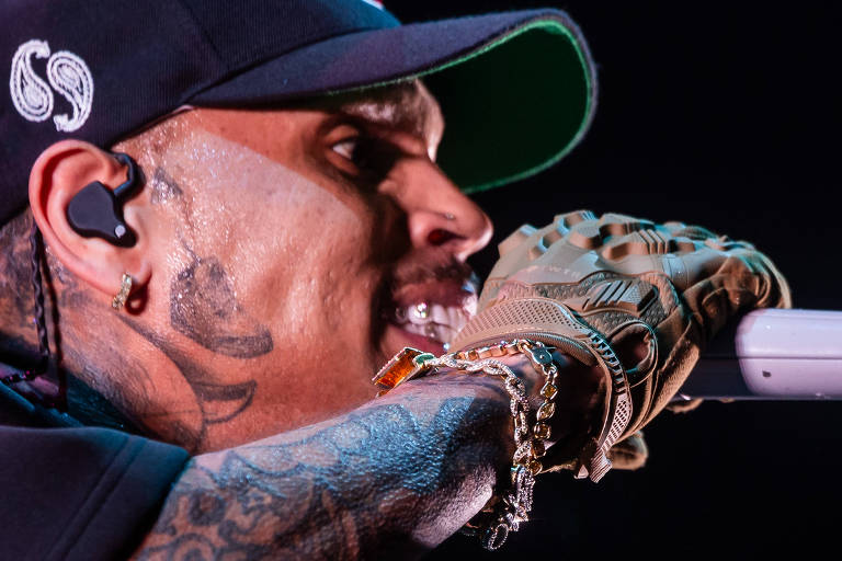 Close no rosto do rapper americano Chris Brown， que segura microfone dirante show. Ele tem tatuagem no rosto e no braço e usa um boné