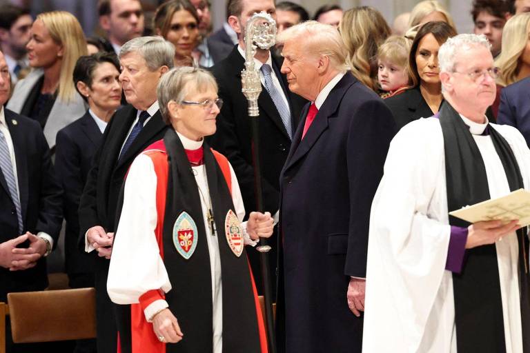 A imagem mostra uma cerimônia com várias pessoas presentes. No centro， Donald Trump está conversando com uma mulher vestida com uma vestimenta clerical， segurando um bastão. Ao fundo， há várias pessoas observando， incluindo homens e mulheres em trajes formais. A atmosfera parece ser de um evento solene.