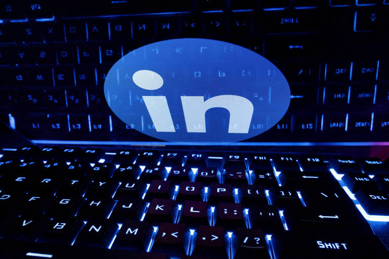 A imagem mostra um teclado iluminado em azul， com o logotipo do LinkedIn em destaque no centro. O fundo é predominantemente azul， e o logotipo é branco， contrastando com a iluminação do teclado.
