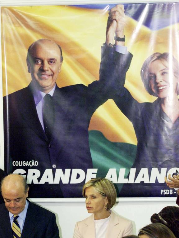 Mesmo com as crises no governo de Fernando Henrique, o PSDB tenta lançar José Serra, que ganhou projeção como ministro da Saúde, à Presidência, citando manter o legado do Plano Real ante supostas mudanças sob Lula; na imagem, Serra concede entrevista sobre a campanha junto da vice, Rita Camata (PMDB)