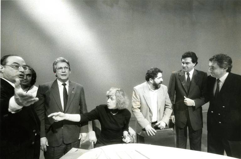 Na foto, Mário Covas (PSDB) participa do primeiro debate entre os candidatos à Presidência em 1989, realizado pela Rede Bandeirantes; além dele estão Paulo Maluf (PDS), a jornalista Marília Gabriela, Luiz Inácio Lula da Silva (PT), Ronaldo Caiado (PSD) e Guilherme Afif Domingos (PL)