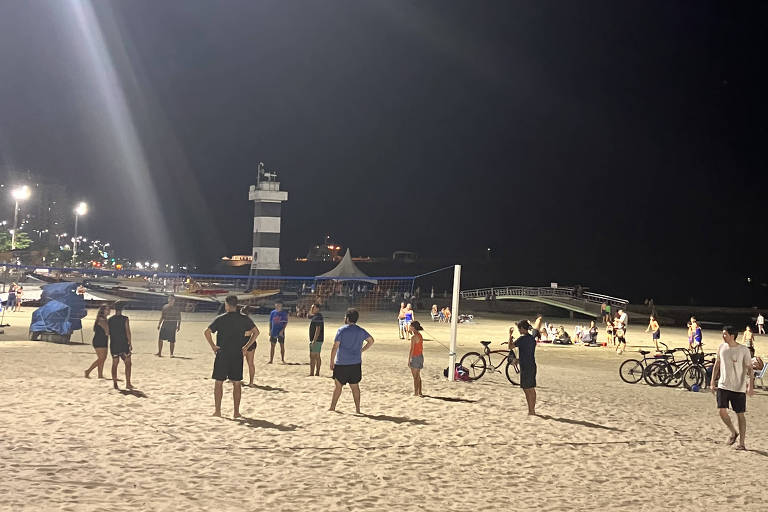 homens de costas em rede de vôlei na praia  pela noite， com luz ao fundo