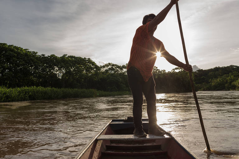 Indígena rema canoa de pé contra o sol