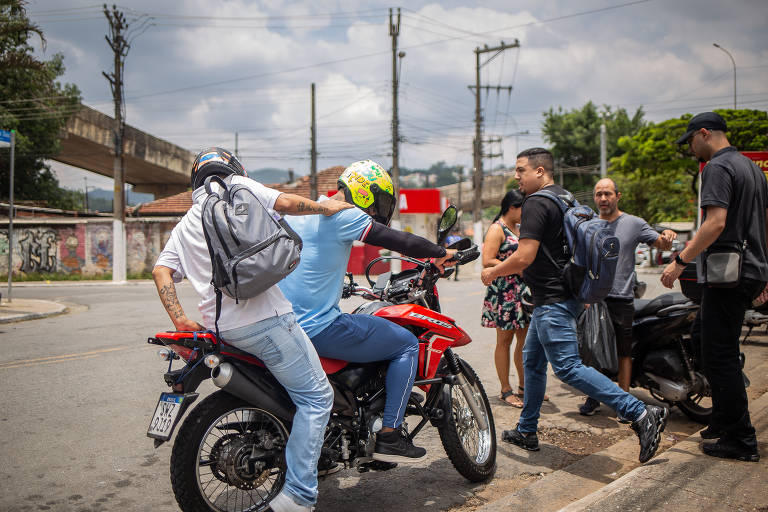 Passageiro sobre na garupa de motocicleta em frente à estação Perus da CPTM, no noroeste de São Paulo; motociclistas prestam serviço de transporte para passageiros mesmo com proibição  da prefeitura