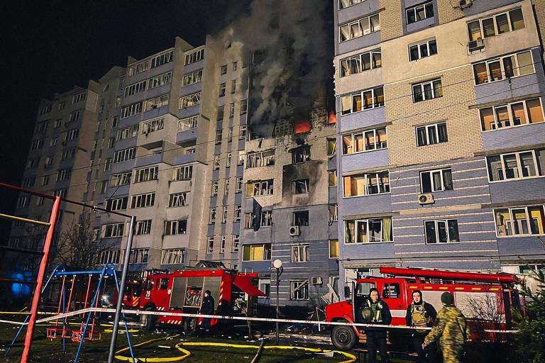 Carros vermelhos de bombeiros em frente a prédio em chamas