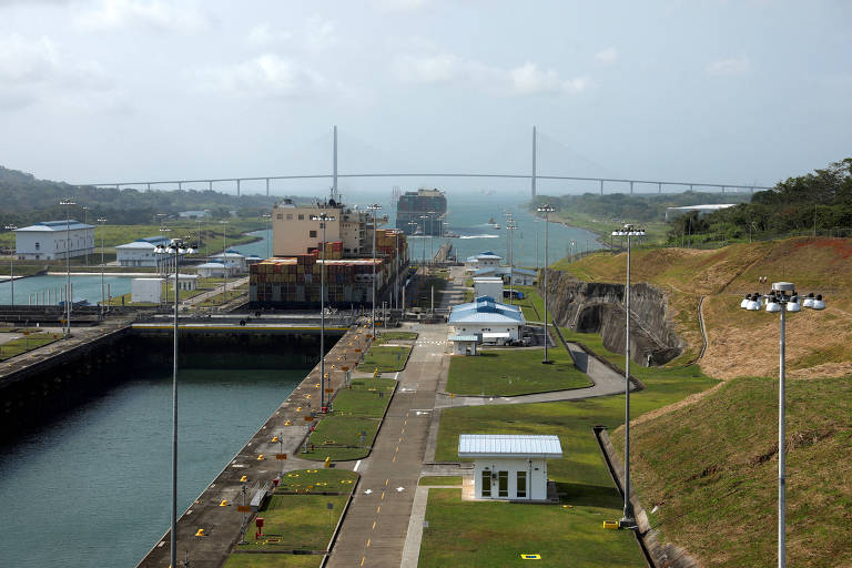 Imagem mostra um trecho do Canal do Panamá， com navios dentro das eclusas， pontes ao fundo e instalações industriais