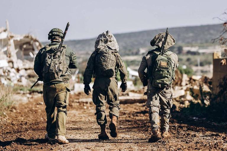 Imagem mostra três soldados com roupas camufladas de marrom e verde em uma estrada de terra