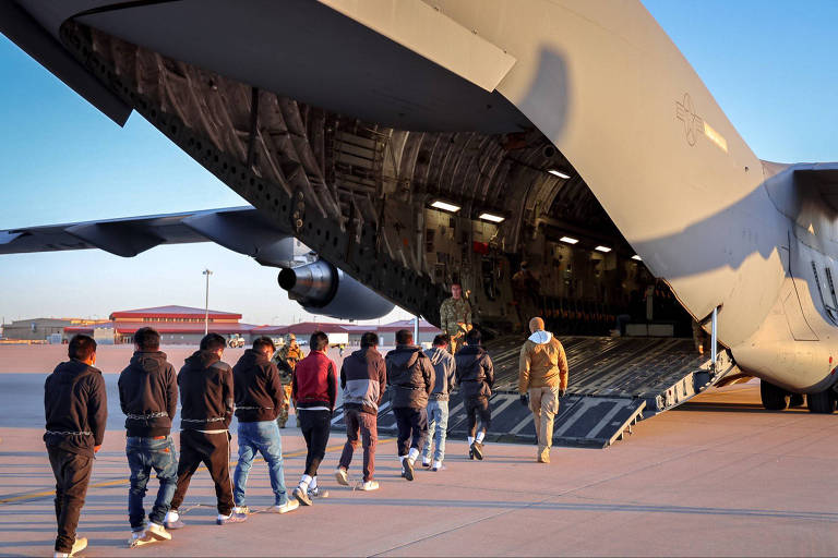 Pessoas em fila entram em avião militar de carga pela abertura traseira da aeronave