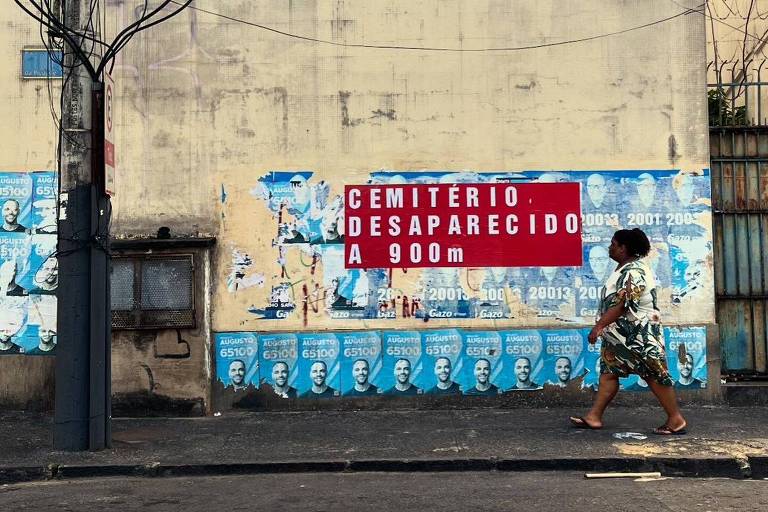 A imagem mostra uma parede amarela， onde estão colados vários cartazes e faixas. Em destaque， uma faixa vermelha com a expressão quot;cemitério desaparecido a 200 metrosquot; em letras brancas