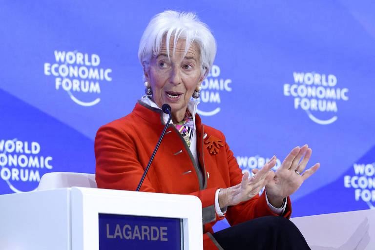 Imagem mostra Christine Lagarde， uma mulher com cabelo curto e branco， vestindo um casaco vermelho， está sentada em um painel durante o Fórum Econômico Mundial. Ela está gesticulando com as mãos enquanto fala， e ao fundo há um painel azul com o logotipo do evento.